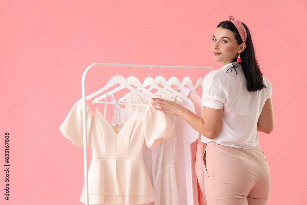 Beautiful young woman choosing clothes on pink background