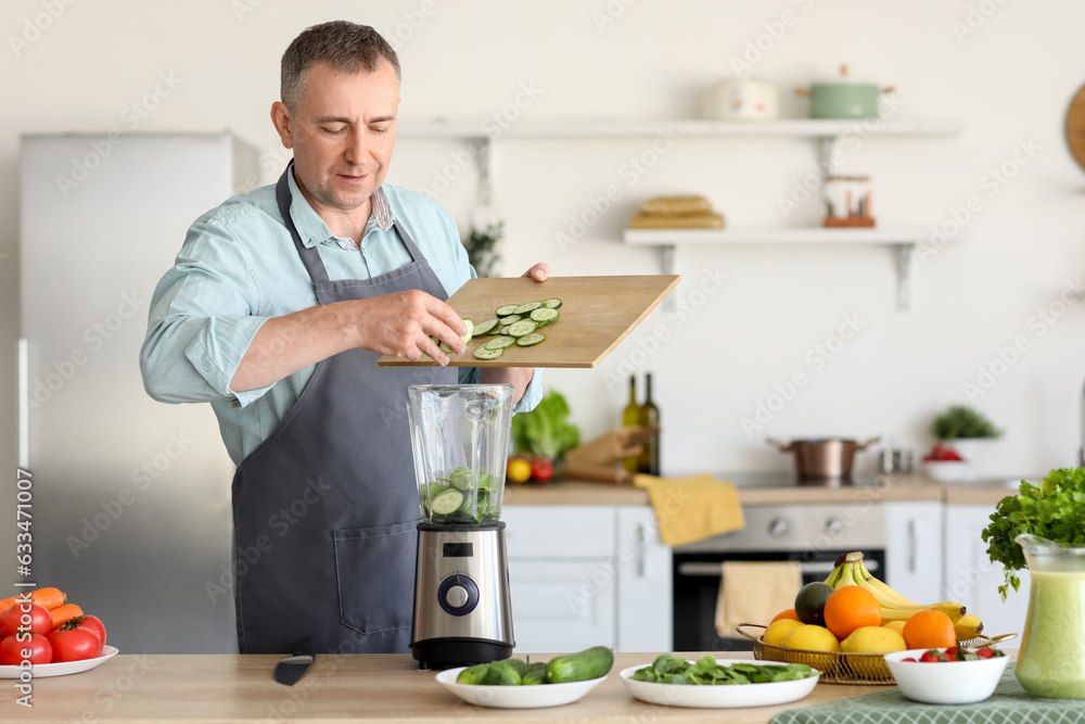 Mature man putting cucumber slices into blender in kitchen