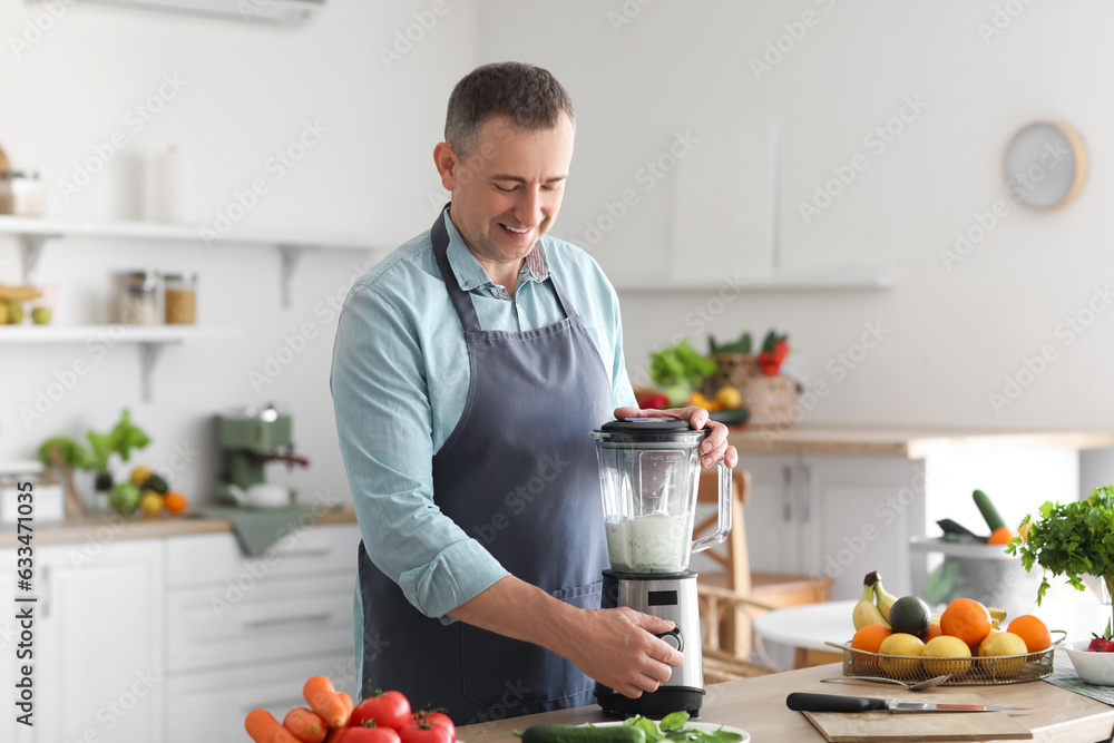 Mature man making smoothie with blender in kitchen