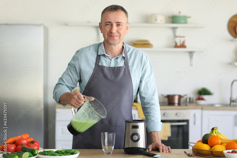 Mature man pouring fresh smoothie from blender into glass in kitchen