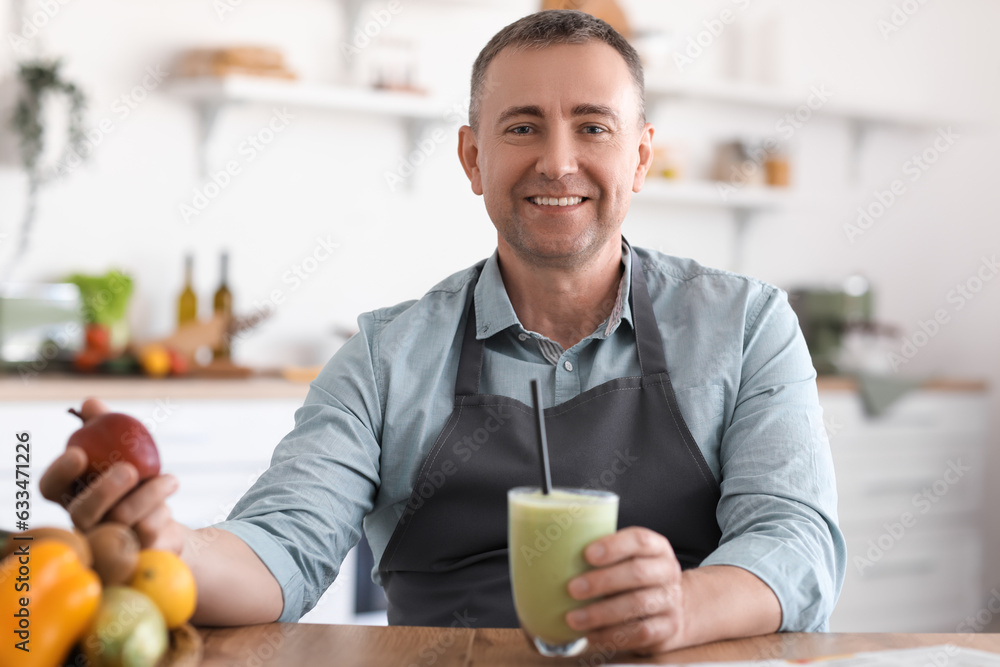 Mature man with glass of fresh smoothie and fruits in kitchen
