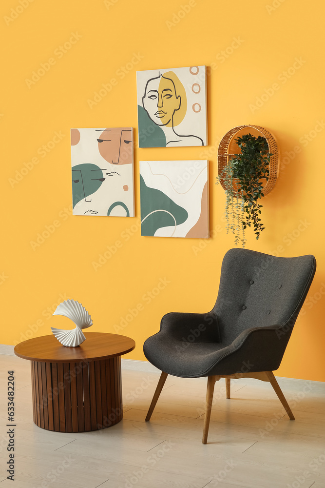 Grey armchair and wooden coffee table near orange wall with different paintings