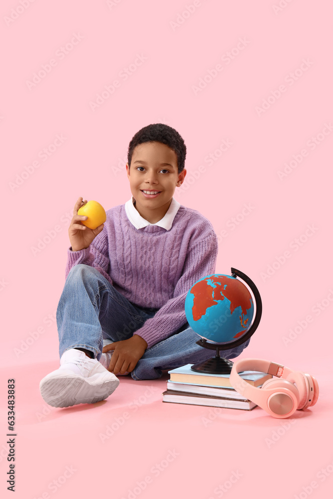 Little African-American schoolboy with globe, books and apple on pink background