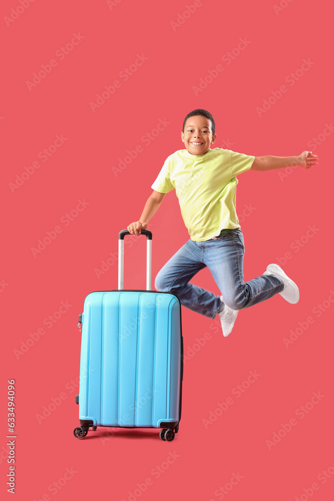 Little African-American boy jumping with suitcase on red background