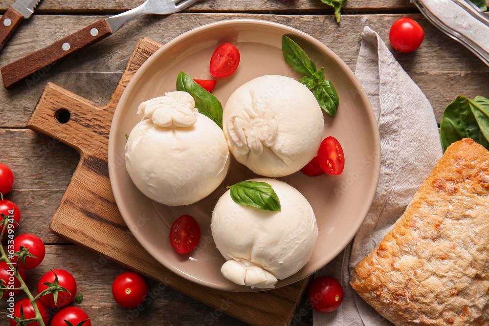 Plate of tasty Burrata cheese with basil and tomatoes on wooden background