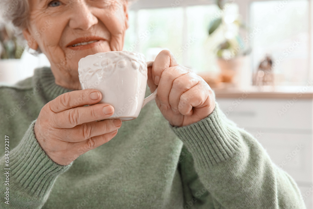 Senior woman drinking tea in kitchen, closeup