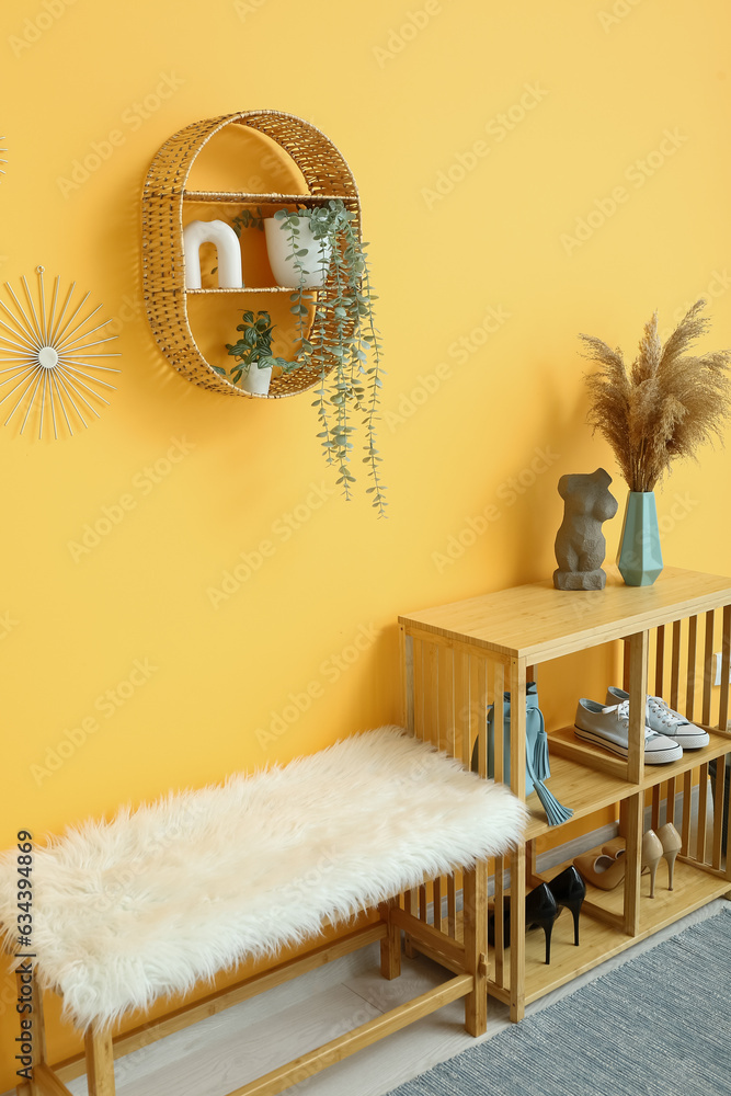 Shelving unit with shoes, shelf and bench near orange wall in hall