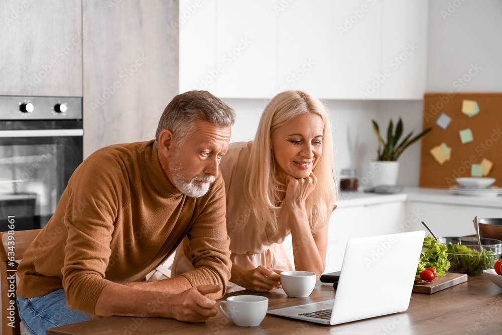 Mature couple with cups of coffee watching video in kitchen