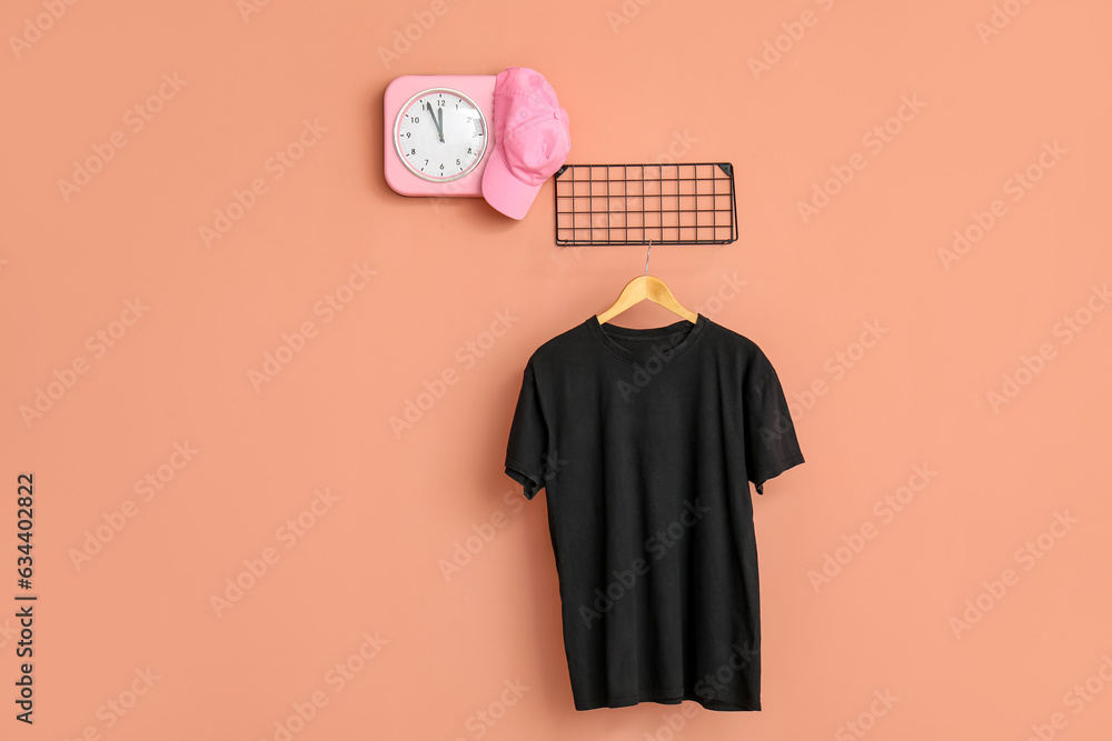 Stylish black t-shirt and cap hanging on pink background