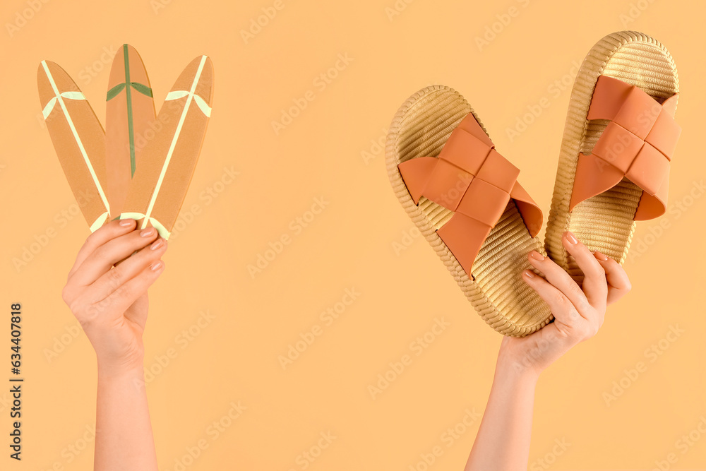 Female hands with mini surfboards and flip flops on orange background