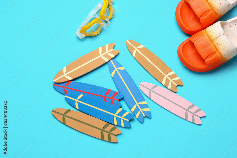 Different mini surfboards, flip-flops and goggles on blue background