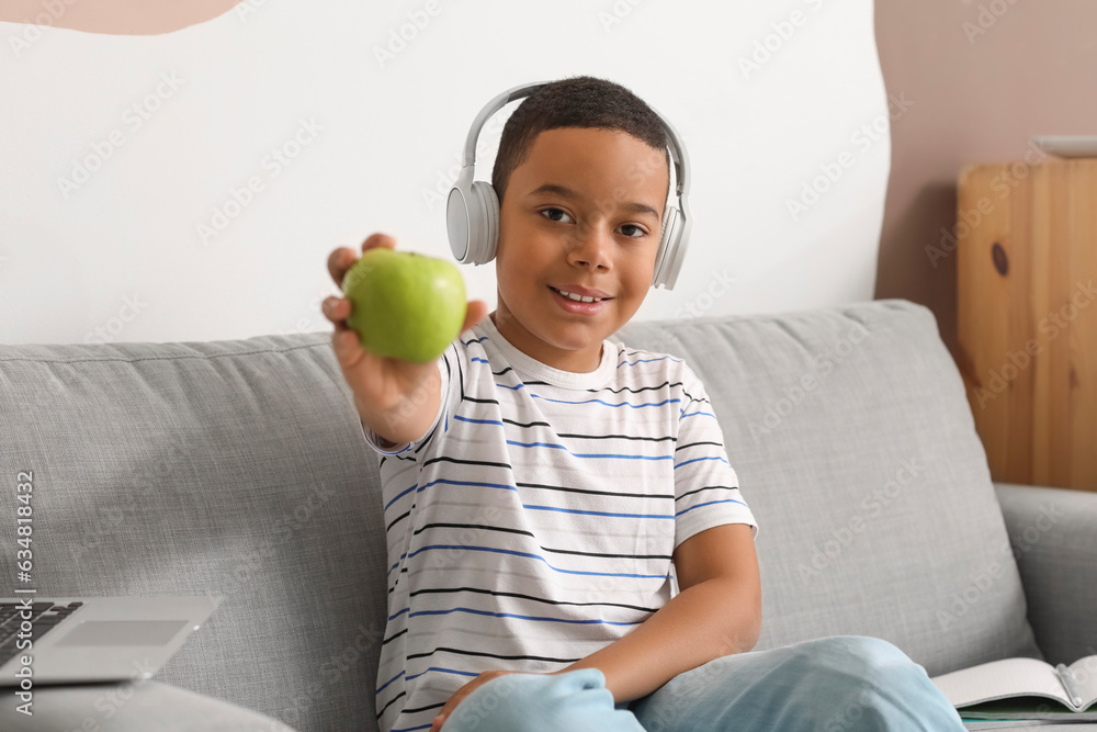 Little African-American boy in headphones with apple studying computer sciences online at home
