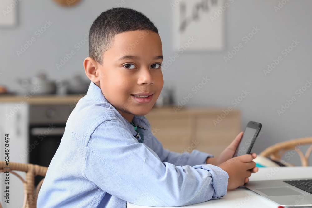 Little African-American boy with mobile phone studying computer sciences online at home