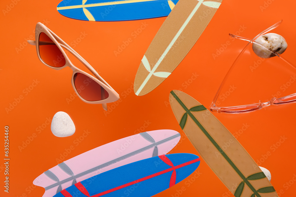 Flying mini surfboards and sunglasses on orange background