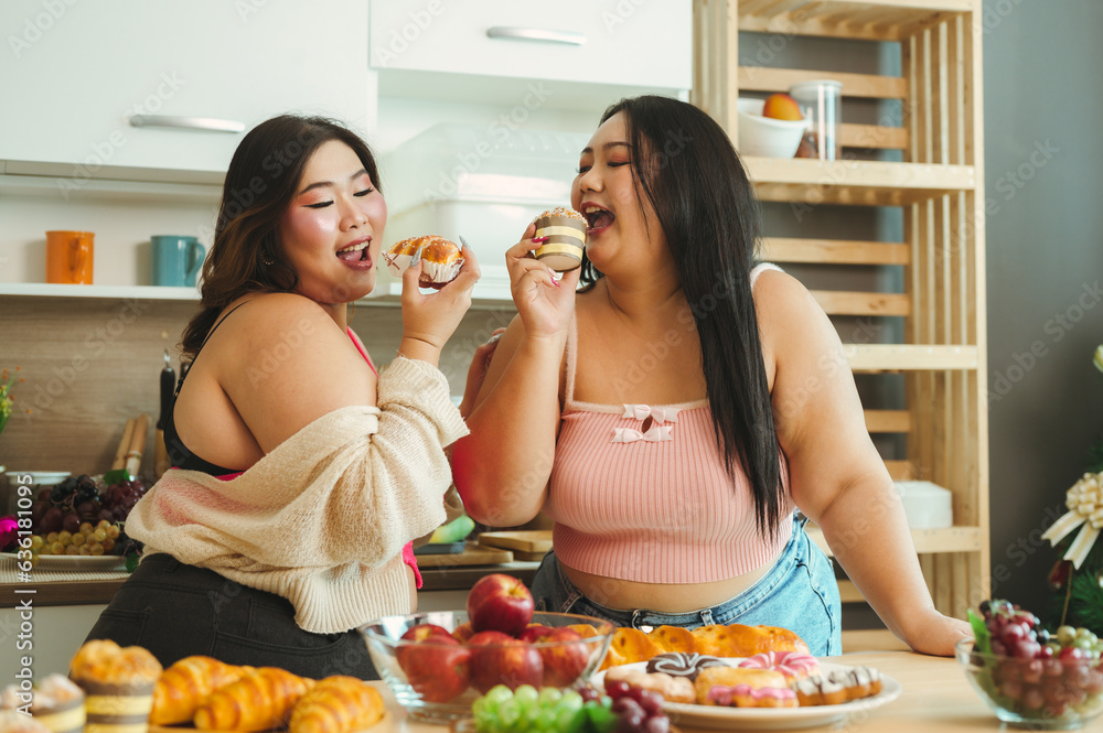 Two fat beautiful Asian women stand happily smiling at the kitchen counter preparing bread and donut