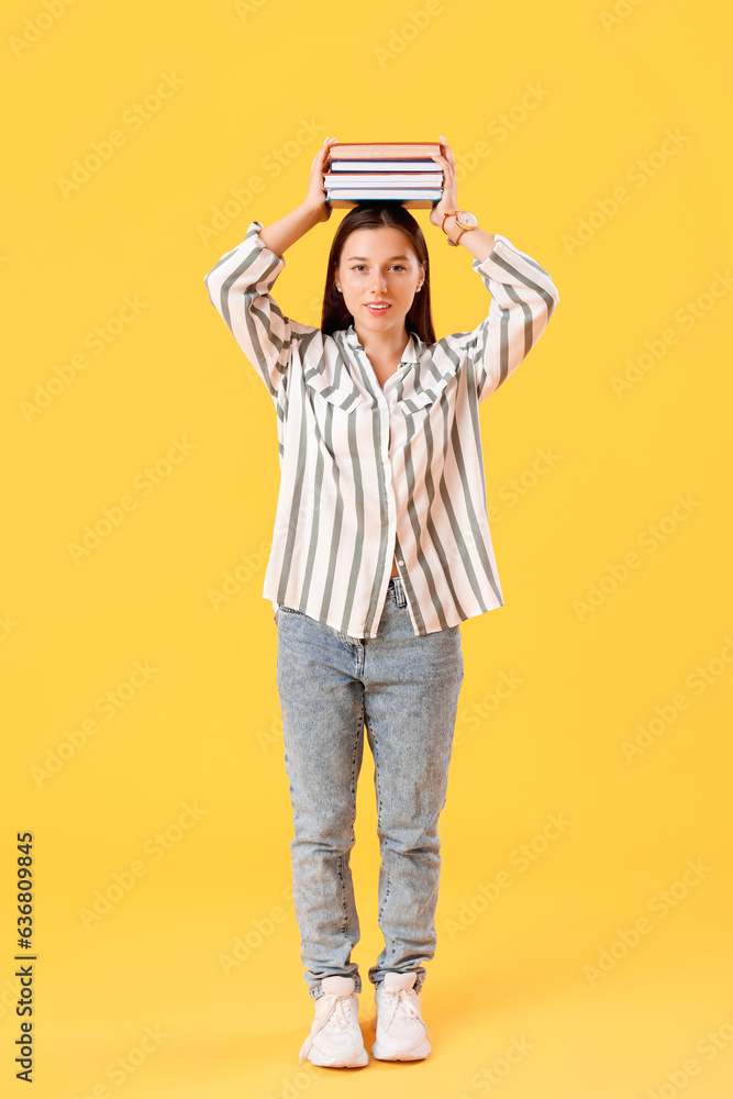 Happy female student with many books on yellow background