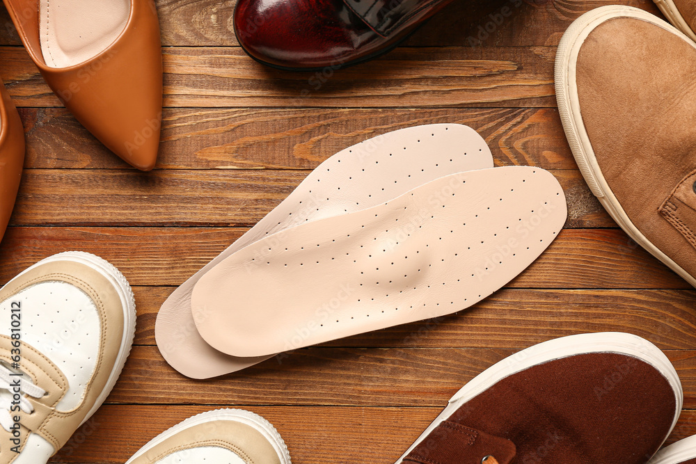 Pair of leather orthopedic insoles and different shoes on wooden background, closeup
