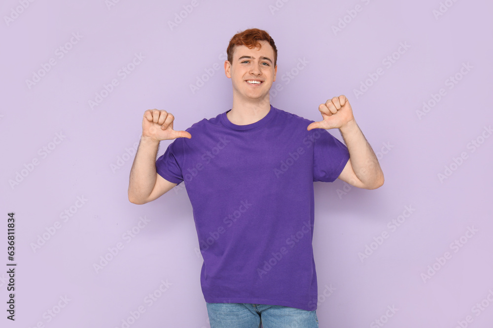 Young man pointing at his purple t-shirt on lilac background
