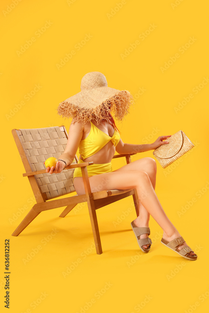 Beautiful young woman in stylish sandals with beach accessories sitting on wicker chair against yell