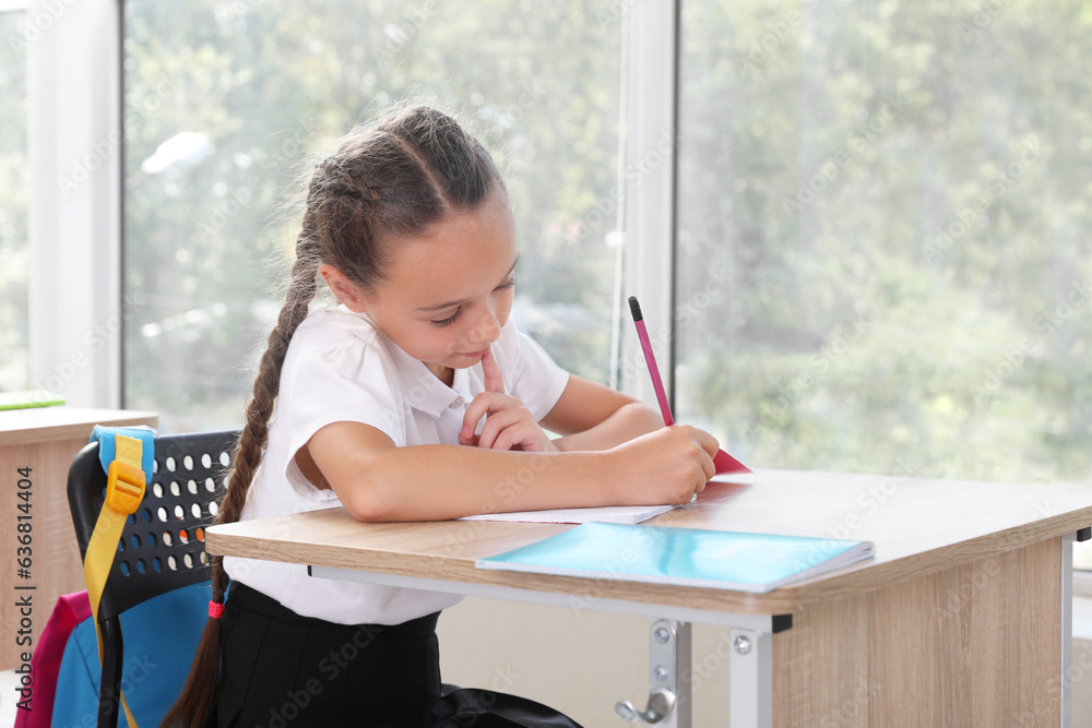Little schoolgirl sitting at desk during lesson in classroom