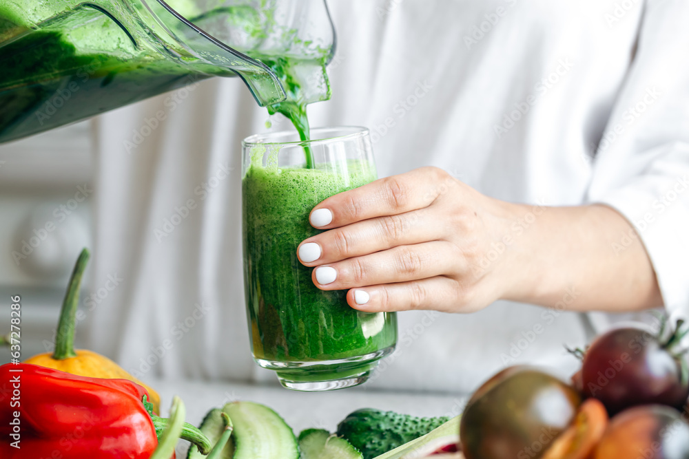 A woman pouring green smoothie to glass, healthy food concept.