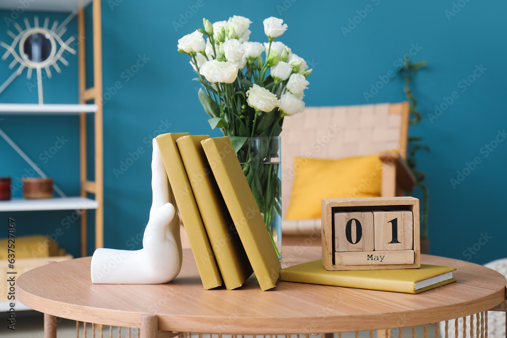 Stylish holder for books with vase of roses on table in room