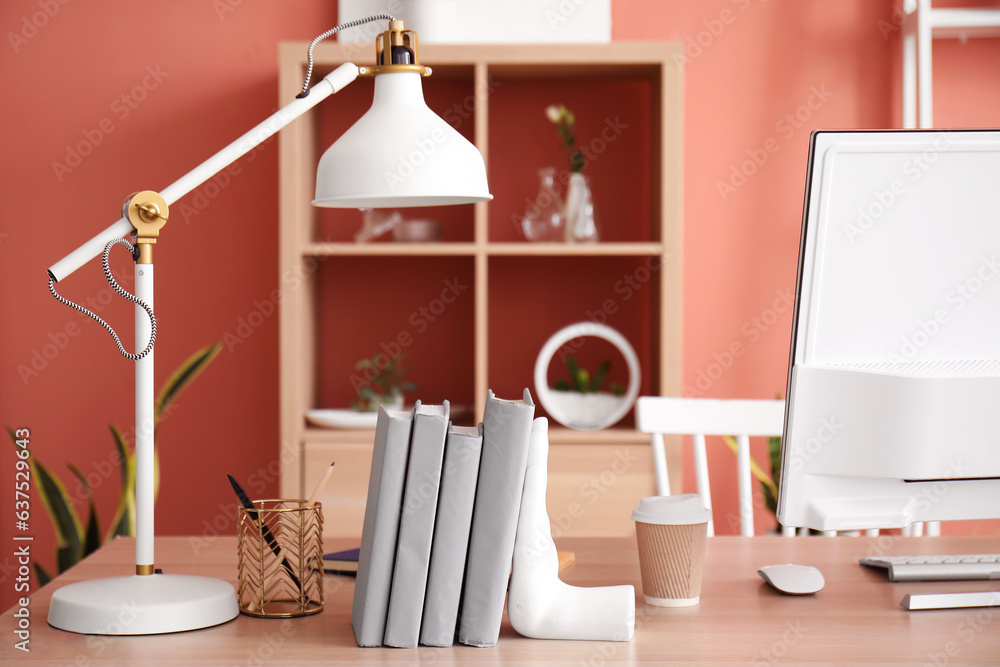 Workplace with computer, stylish holder for books and lamp in room