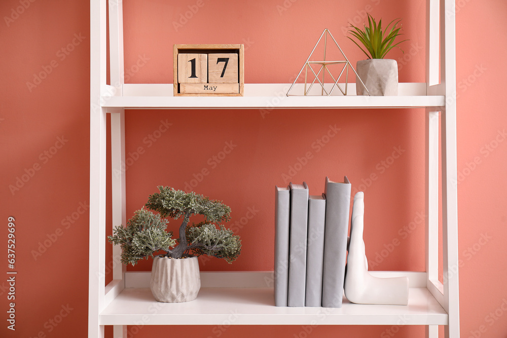 Shelving unit with holder for books  and bonsai tree near color wall