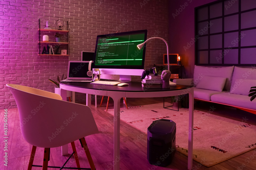 Programmers workplace with computer, laptop and glowing lamp in dark office