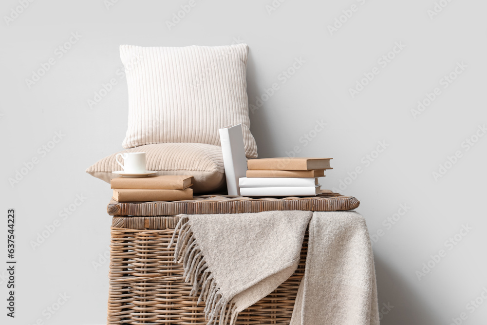 Books with cup and pillows on basket near light wall