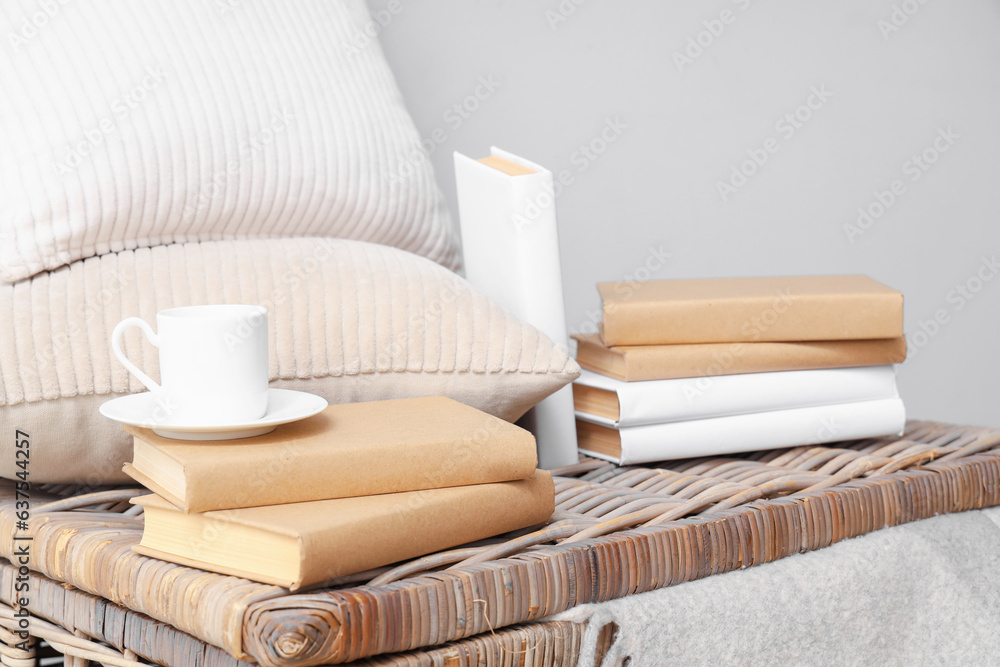 Books with cup and pillows on basket near light wall, closeup