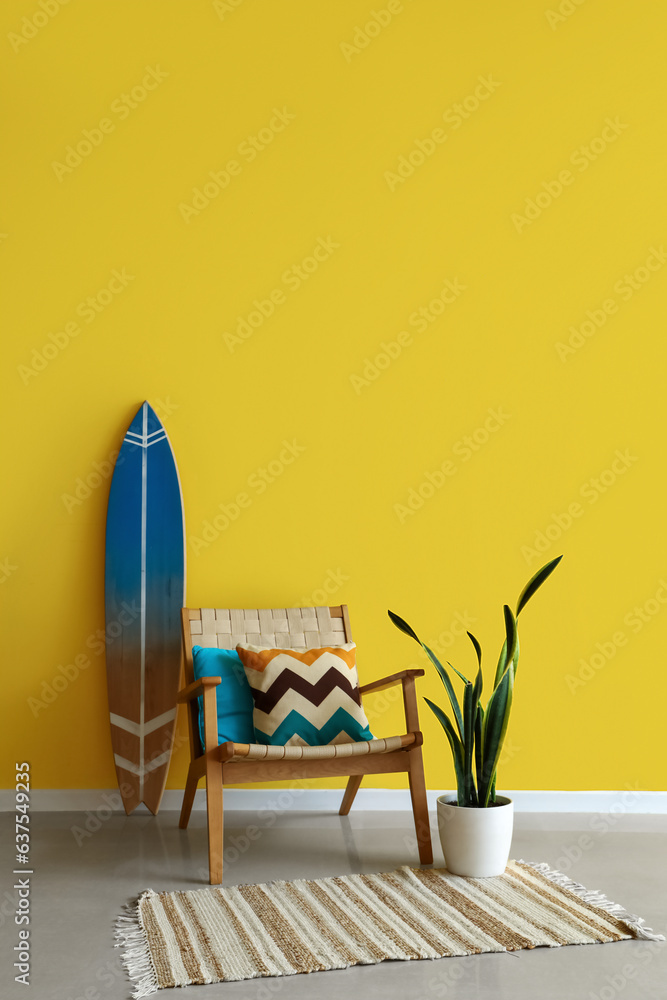 Stylish armchair, surfing board and houseplant near yellow wall