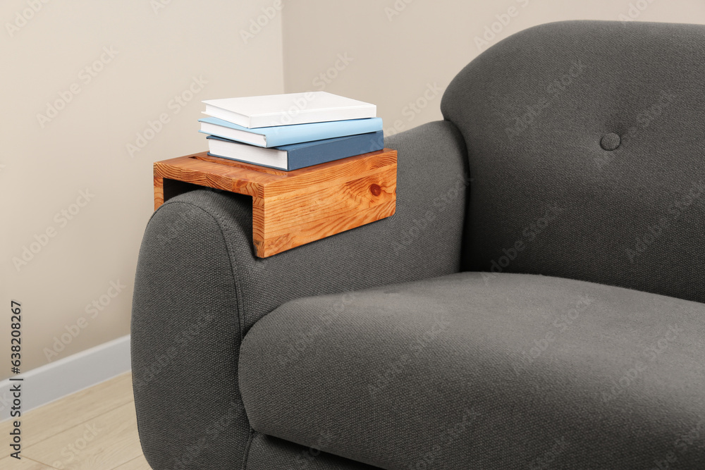 Books on sofa with wooden armrest table in room. Interior element