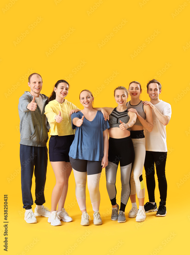 Group of sporty young people showing thumbs-up on yellow background