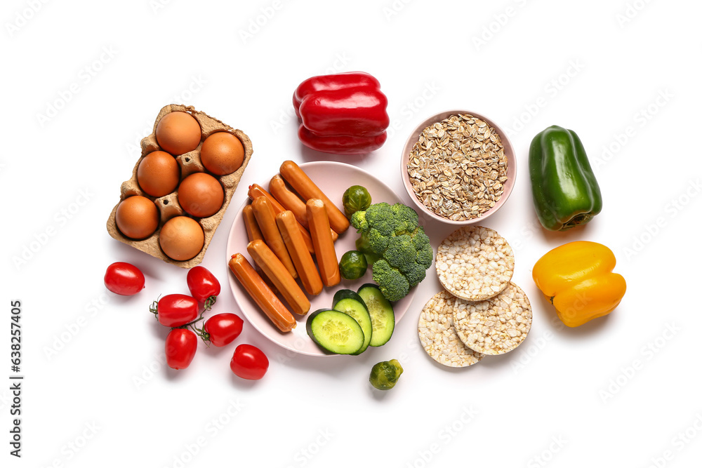 Plate of sausages, fresh vegetables with eggs in package and oatmeal on white background