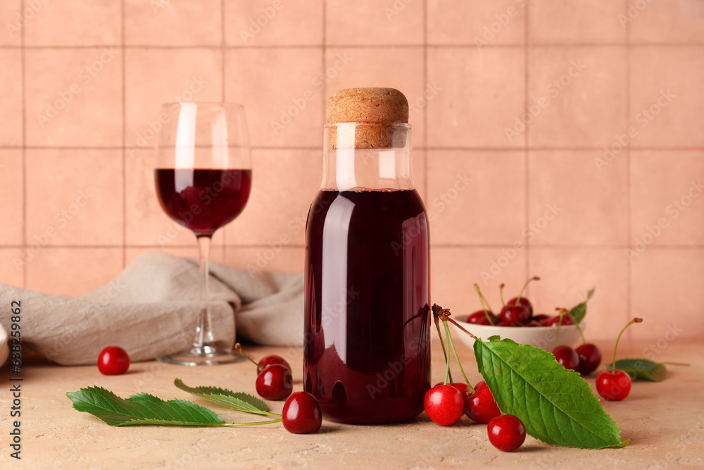 Bottle and glass of sweet cherry liqueur with berries on table near beige tile wall