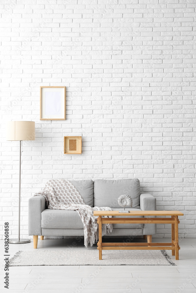 Light wooden coffee table with couch and floor lamp near white brick wall