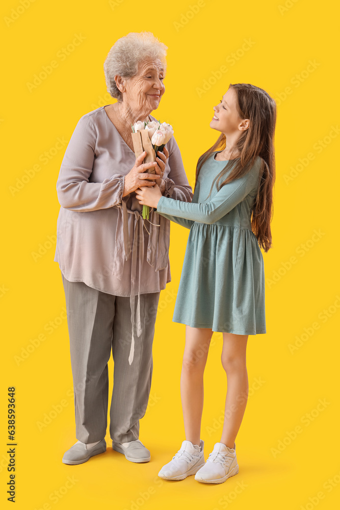 Little girl greeting her grandmother with flowers on yellow background