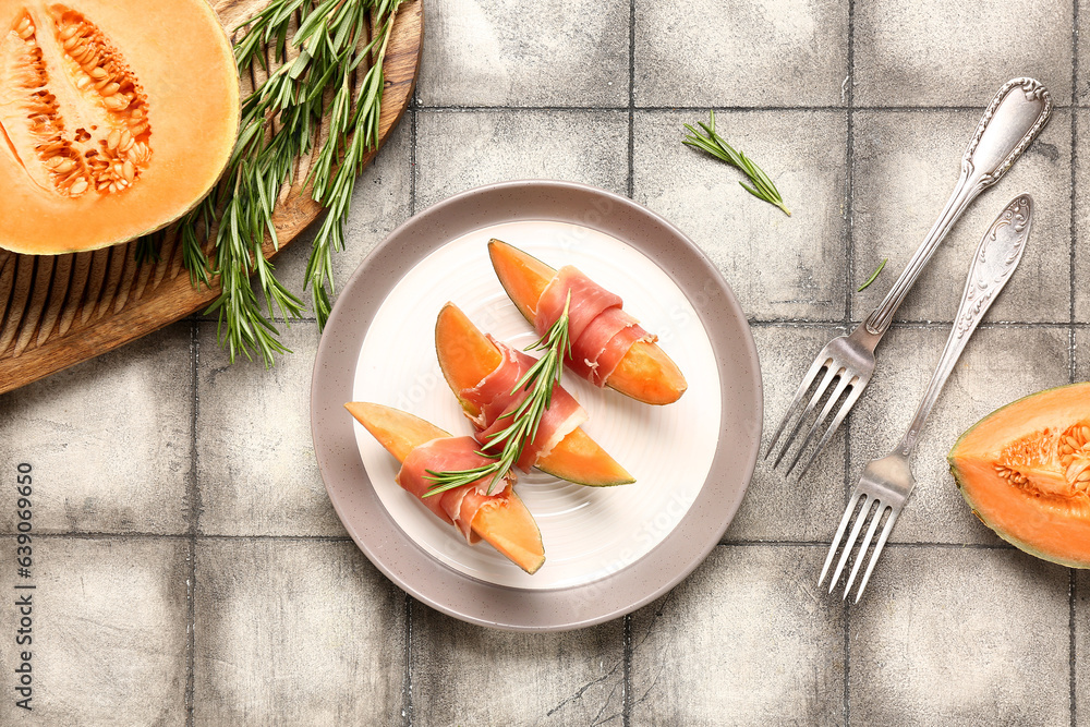 Plate of delicious melon with prosciutto and rosemary on grey tile background