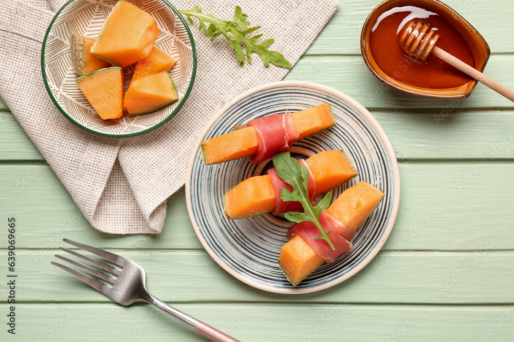 Plate of delicious melon with prosciutto and arugula on green wooden background