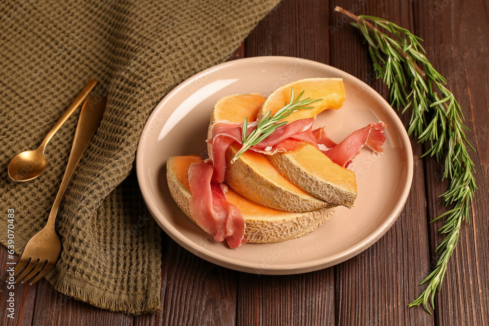 Plate with tasty melon, prosciutto and rosemary on dark wooden background