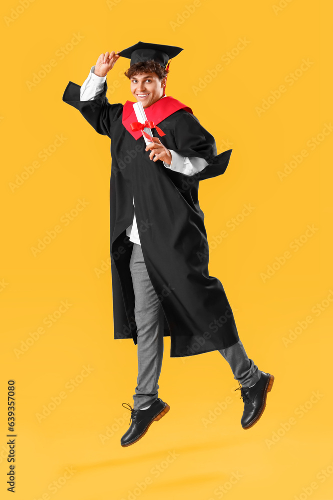 Male graduate student with diploma jumping on yellow background