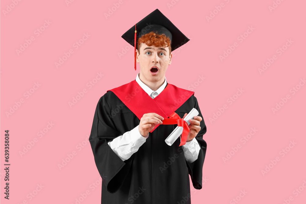 Shocked male graduate student with diploma on pink background