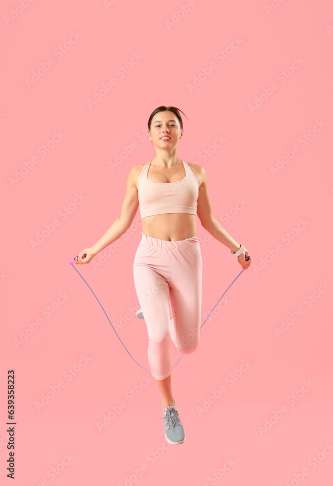 Sporty young woman jumping rope on pink background