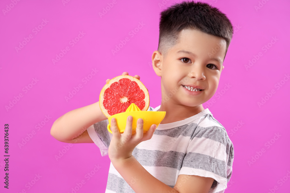 Little Asian boy with slice of fresh grapefruit and juicer on purple background