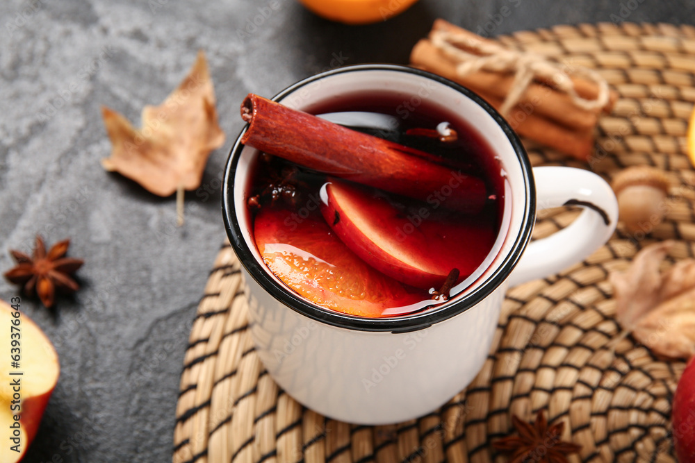 Cup of hot mulled wine with apple and orange on black background