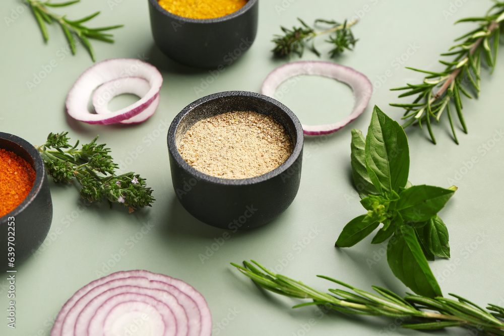 Bowls of aromatic spices, onion and herbs on color background, closeup