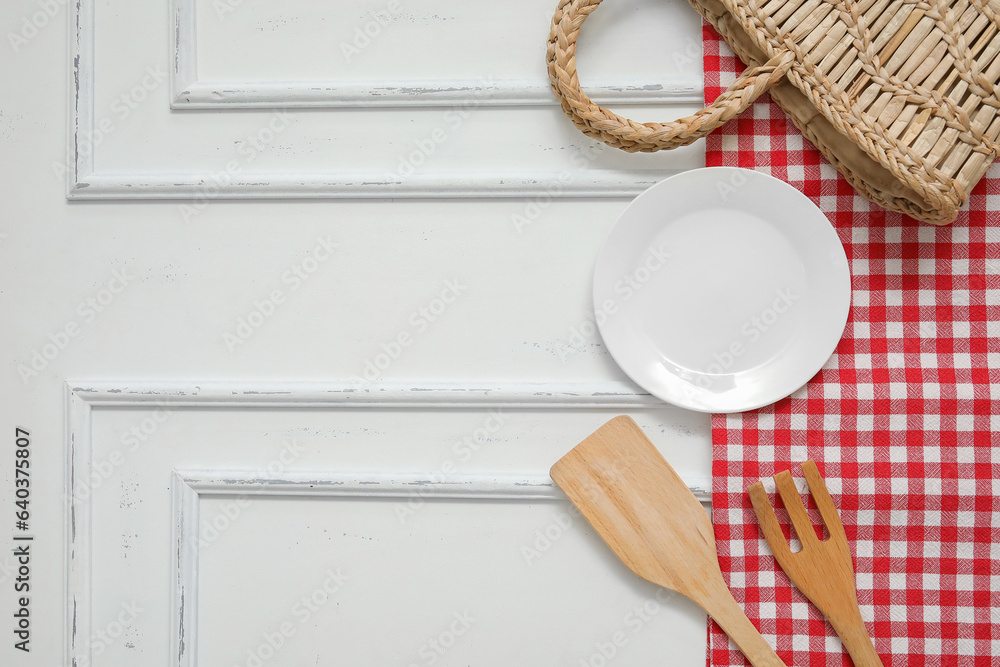 Clean plate, fork, spatula, wicker bag and napkin on white wooden background