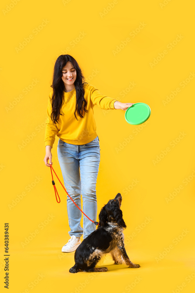 Young woman with cocker spaniel playing frisbee on yellow background
