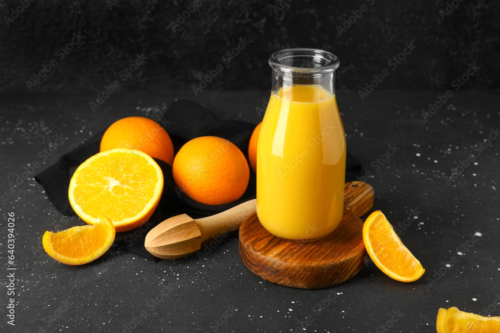 Wooden board with bottle of fresh orange juice and juicer on black background